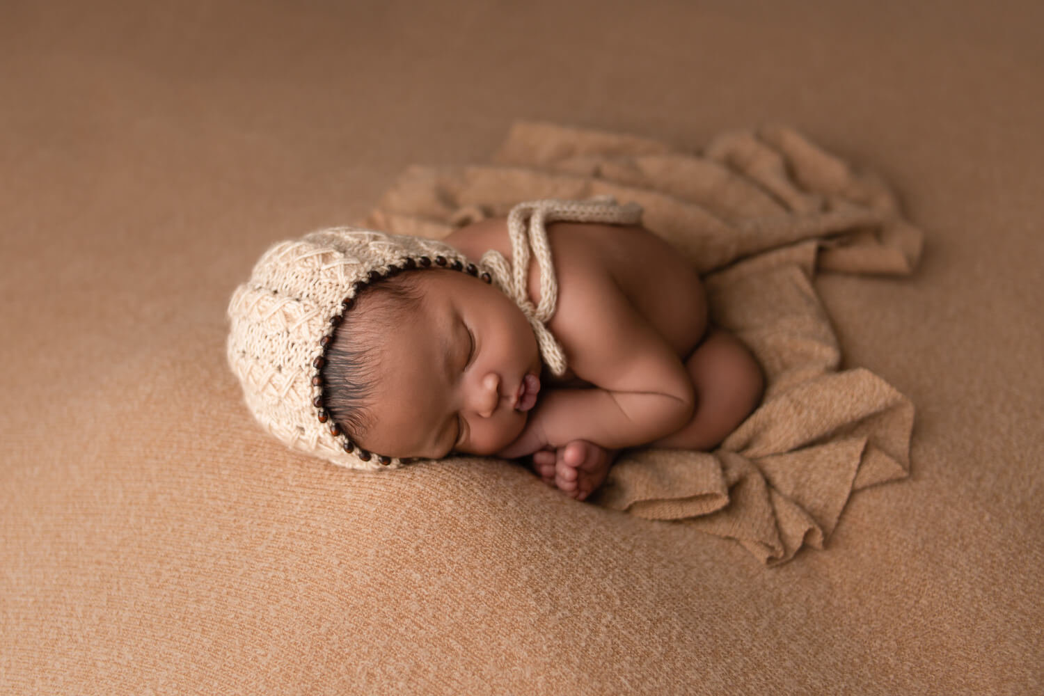 newborn baby with bonnet laying on bed