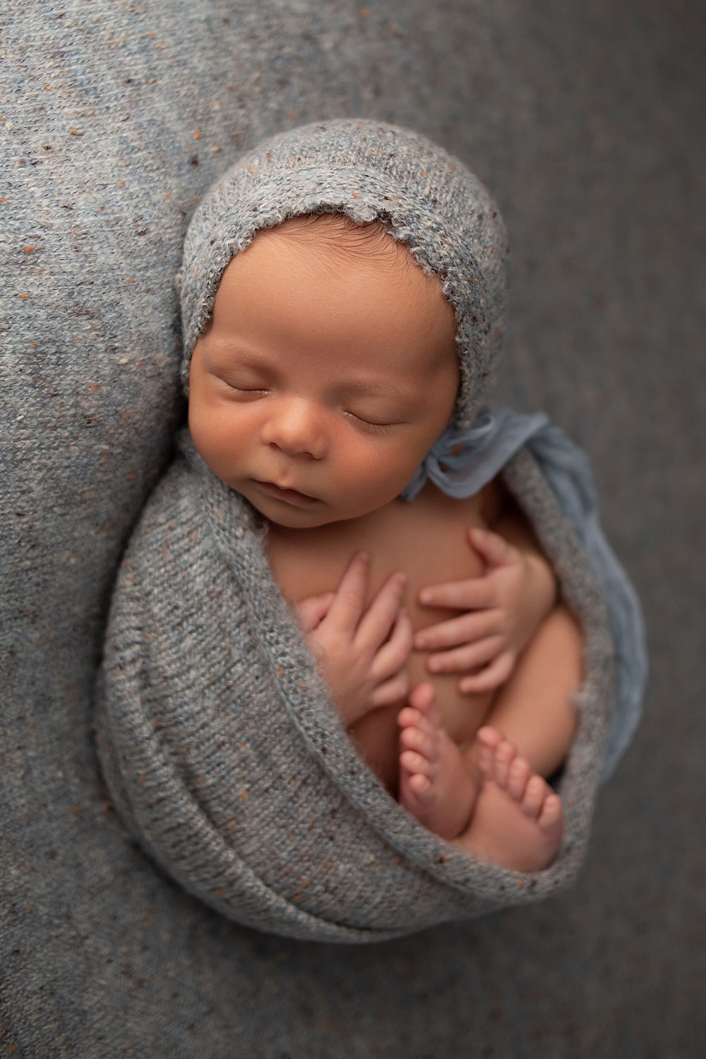 newborn-posed-on-gray-backdrop-with-bonnet