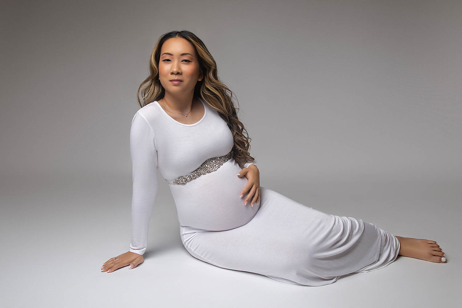 Pregnant woman wearing white dress for maternity sitting on floor in pembroke pines, fl