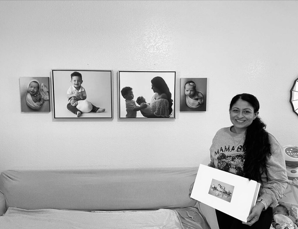 mom holding an album standing next to a wall gallery of photos taken from her baby's newborn photography session in pembroke pines fl