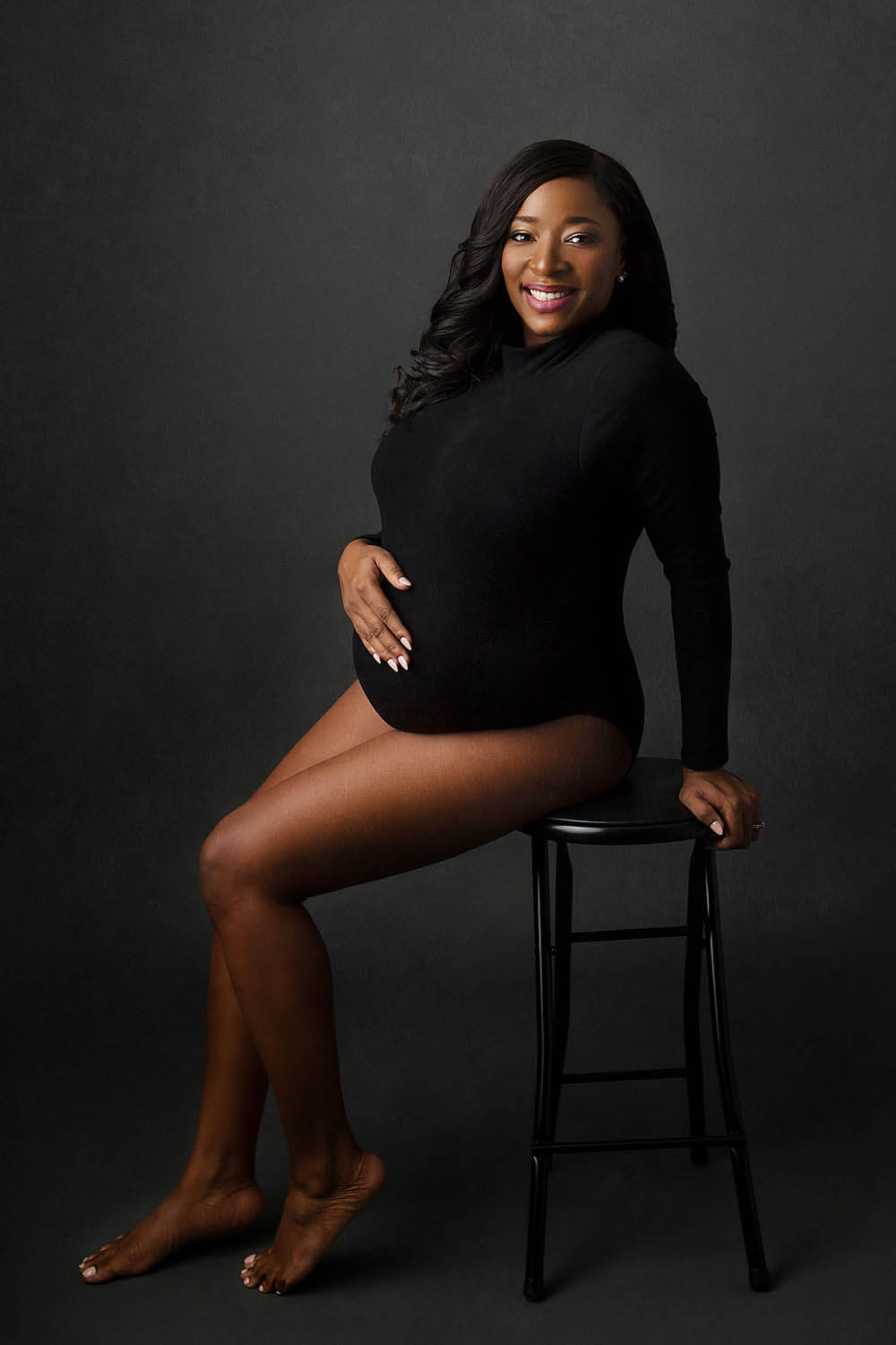 black woman in bodysuit sitting on a stool for her maternity photoshoot in the Miami area near ft lauderdale fl