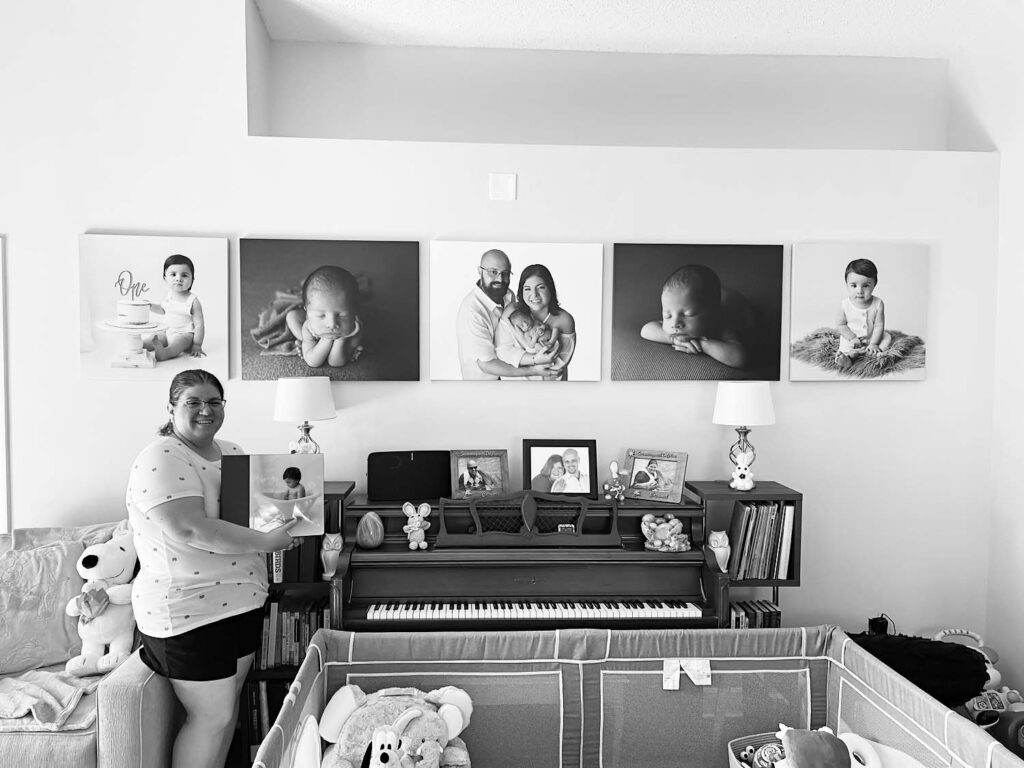 mom holding her album and standing next to her wall photos from her baby's photoshoot in miami fl